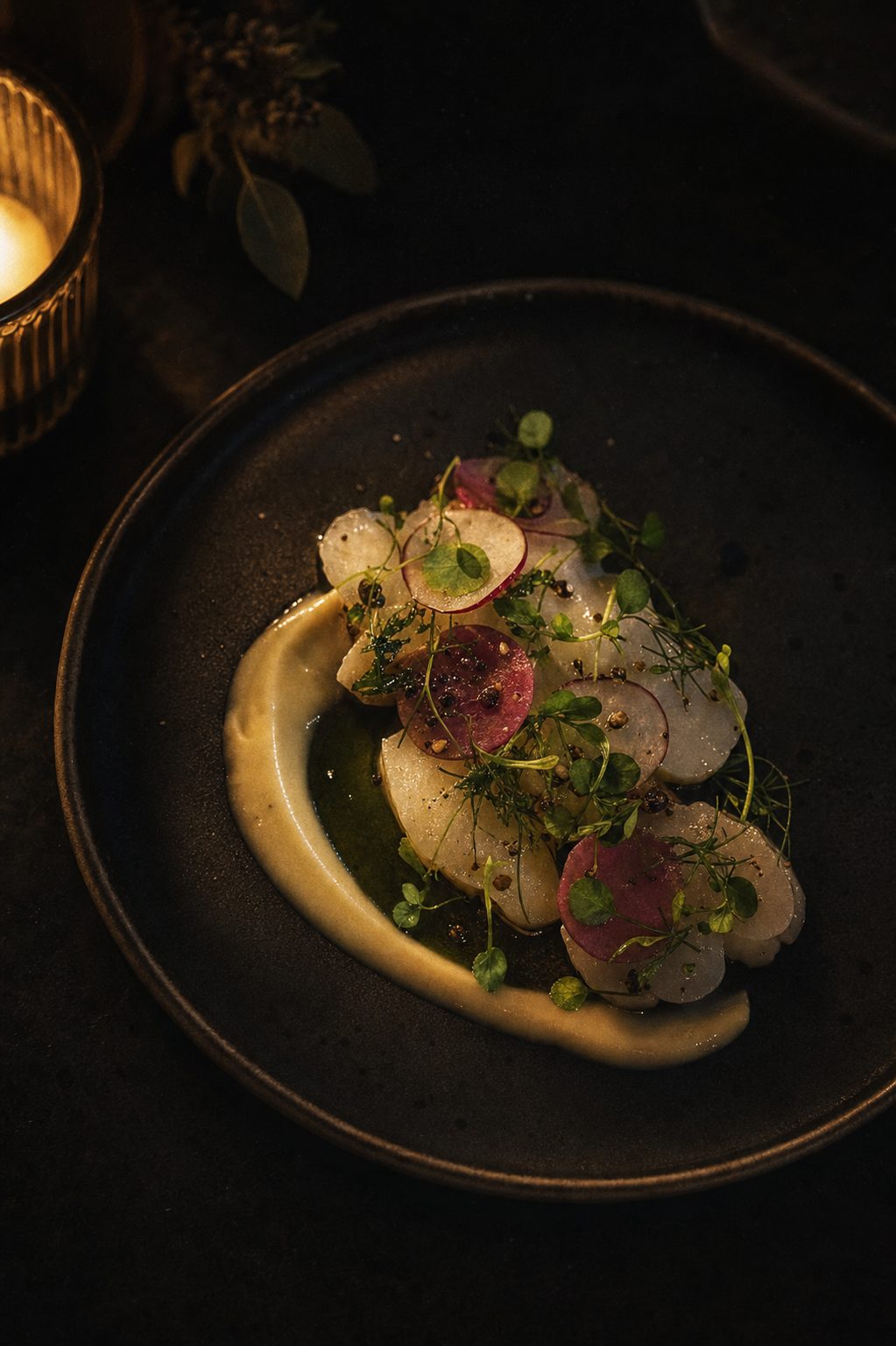 A single plated course on a dark table, lit by low candlelight